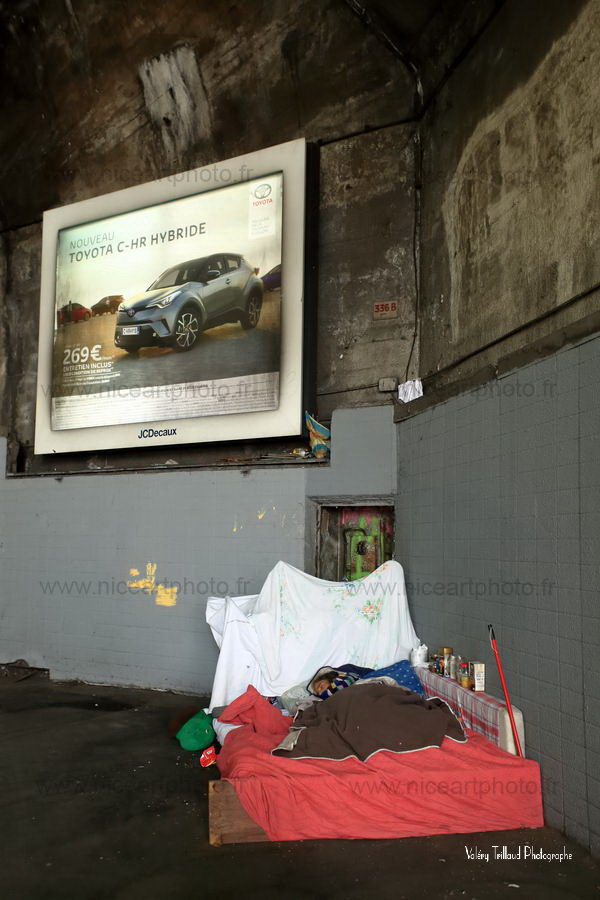 Personne sans domicile fixe allongée sur un lit improvisé sous une enseigne publicitaire